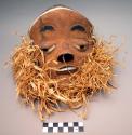 Carved wood mask with brown, black, and white painted realistic face with raffia