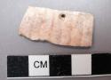 Piece of carved cardium shell with perforation. 3.3 x 1.6 cm.