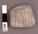 Piece of burned cardium shell, rounded edges, quadrangular. 2.7 x 2.5 cm.