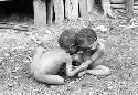 Samuel Putnam negatives, New Guinea; 2 children; very small boy playing in a sili; heads are together and they hold each other's hands