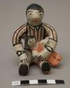 Storyteller figure man wearing watch and striped shirt, seated with child on lap; signed S. Ortiz