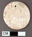 Carved shell disk (cardium?) with single perforation near one edge. 3.4 x 3.3.