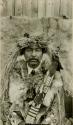Thompson River Indian man "Tu.z.lExeskEt" in costume, in front of fur blanket