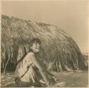 Photograph album, Yaruro fieldwork, p. 67, photo 1, girl sitting outside thatched hut smiling