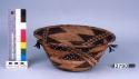 Coiled basket, brown woven design with feather and shell ornament.