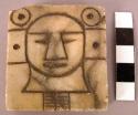 Ground stone sculpture, square with carved human head & geometric designs
