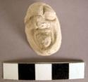 Cast of moulded and incised human head, facial features, tongue out, nose missin