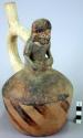 Ceramic bottle, stirrup spout, human effigy, molded head and body, sitting cross