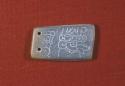 Small flat piece of jade with an incised design on one side.  Two perforations a