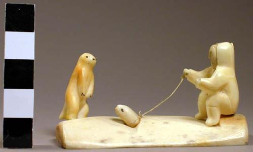 Ivory carving - man sitting pulling a seal from the water and a polar bear