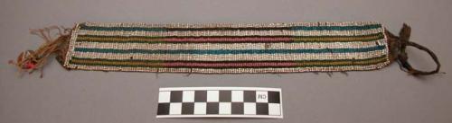 Woven beaded strip with remnants of cloth at each end.