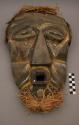 Carved wood mask with black, white, and yellow painted deocrations; fur and raff