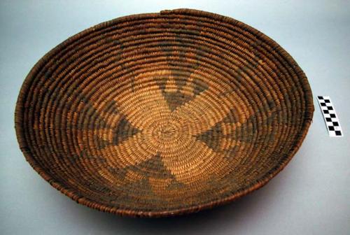 Red coiled flat based basketry bowl. Thick coils with rough stitching