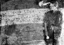 Elizabeth Marshall Thomas standing next to drawings made by children on a wall inside a hut