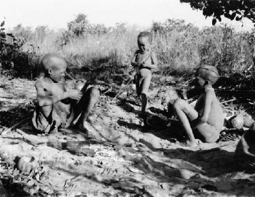 Two people sitting, with a child standing, holding a bow next to them