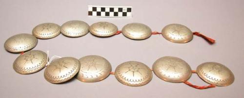 12 circular German silver conchos connected with red rag. Several star designs