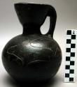 Black jug with handle and incised design, 18 cm h.  diam. of rim: 8 cm.  Diam of
