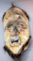 Carved wood mask with yellow and white painted geometric designs and fur trim