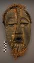 Carved wood mask with yellow and white painted decorations; fur and raffia trim