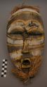 Carved wood mask with yellow and white painted decorations and raffia trim