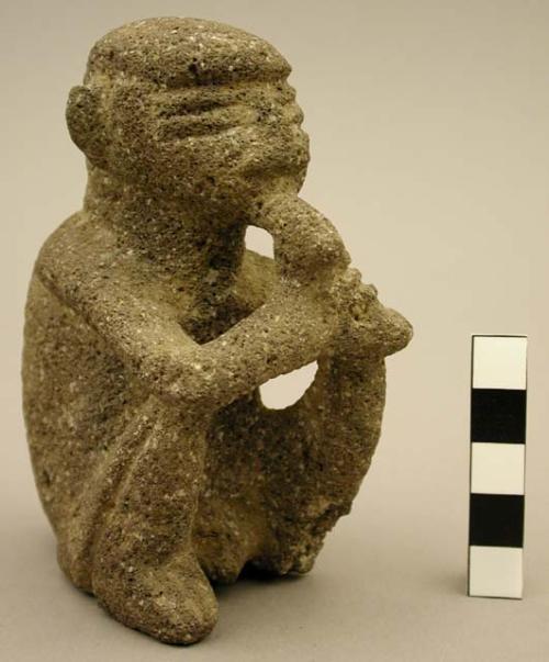 Carved groundstone "Sukia" figure, seated male holding tube