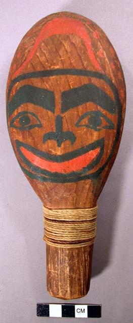 Rattle of light wood and faces painted on each side with black and red