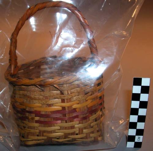 Woven basket of split cane with handle, red and yellow square base, round rim