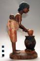 Wood carving of woman with baby on back, brewing sorghum beer in a pot over a fire.