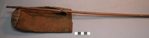 Rough leather bag attached to wood stick. Stick notched at both ends.