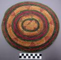 Circular basketry tray of green, purple, and natural color with triangular desig