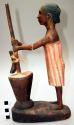Wood carving of woman pounding corn in a wooden mortar