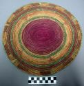 Circular basketry tray of green, purple, natural color, purple center
