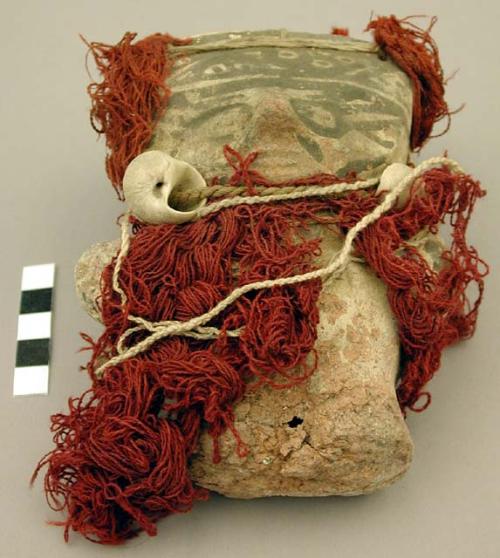 Ceramic figurine wrapped in textiles, some strung with shells, loss on body