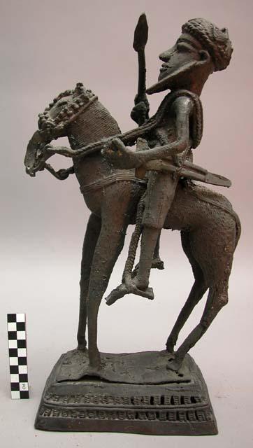 Long legged horse surmounted by rider holding bent spear