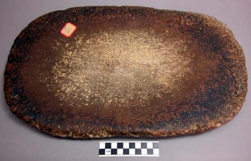 Metate, oval flat stone, worn concave surface with traces of food residue