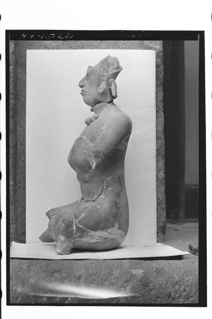 Seated clay figure; crossed legs, one arm missing
