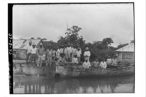 Group of men in boats on bank of river.