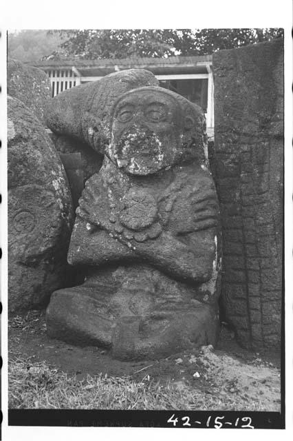 Large seated figure of stone with arms crossed on breast. Mouth damaged