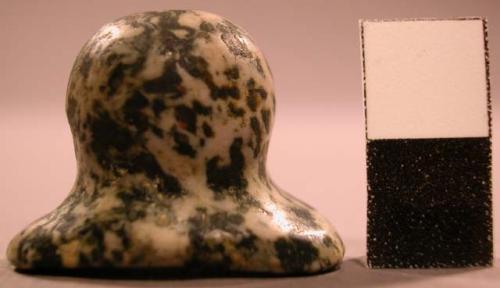 Flaked syenite labret. Head is oval, lared, and concave. Shaft is grooved.