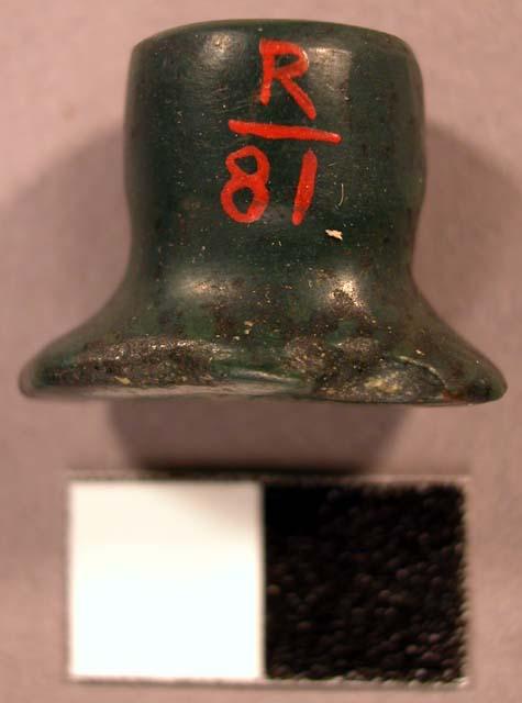 Ground nephrite labret. Head is oval, flared, and flat. Shaft is flat, straight.