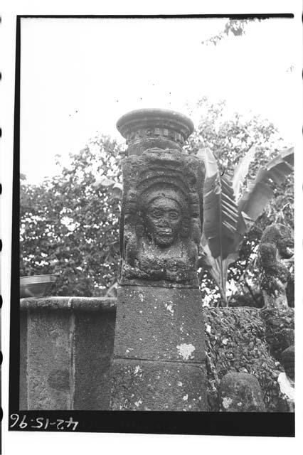 Front view of snake's head with face in jaws. Behind aboriginal stone column