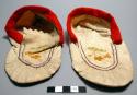 Pair of woman's moccasins of thin white caribou skin bound with red flannel.