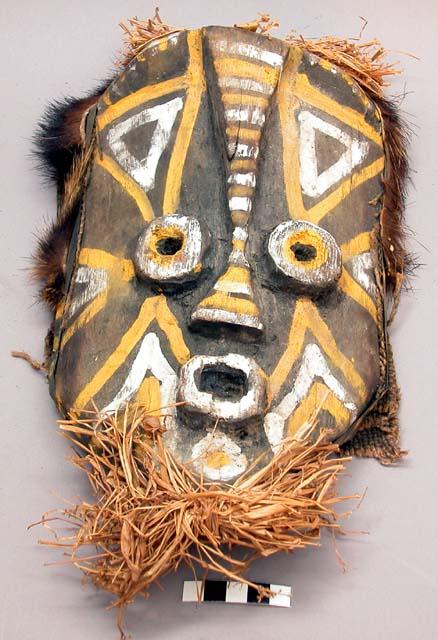 Carved wood mask with black and yellow painted decorations; raffia, fur and fabr