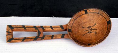 Wood spoon with circular bowl and black and red designs.