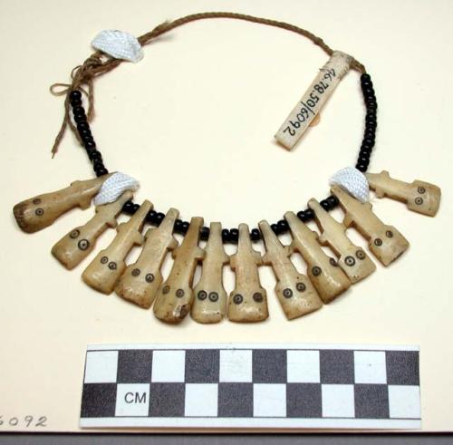 One necklace of small black beads and flat pieces of incised ivory