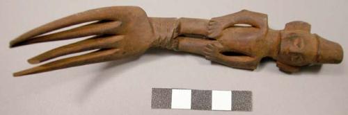 Wooden fork, 4 prongs, handle carved in human effigy: hands resting on flexed kn