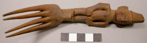 Wooden fork, 4 prongs, handle carved in human effigy: hands resting on flexed kn