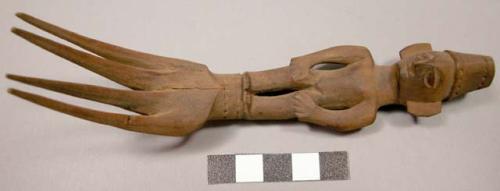 Wooden fork, 4 prongs, handle carved in human effigy: hands resting on flexed kn