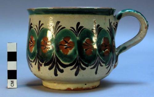 Mug. Red clay, whitish glaze with design in green, rust, and dark brown.