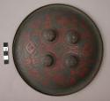 Round, brass shield with four circular brass pieces riveted near +